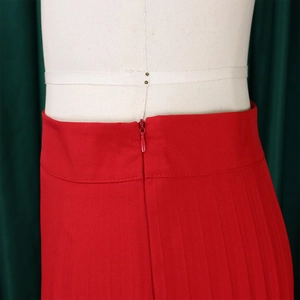 Detailed macro shot of the high waist invisible zipper and pleated texture on the red trousers