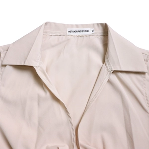Detail of V-neck collar with logo tag on a beige long sleeve wide-leg jumpsuit for women