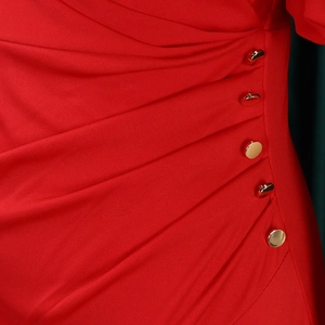 Detail of red dress featuring side pleats and five gold metal buttons on textured fabric