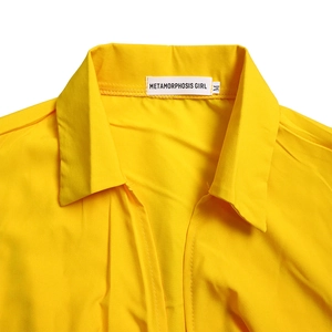 Detail shot of the V-neck collar and woven brand label on a yellow pleated jumpsuit