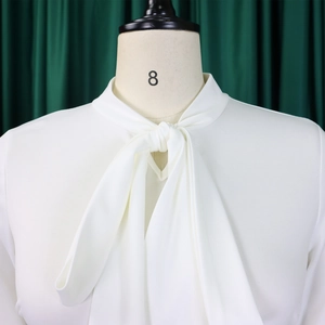 Close-up detail of white chiffon blouse featuring an elegant bow tie neck on a mannequin