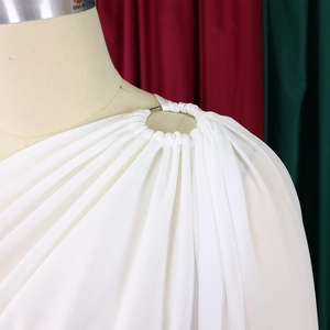 Detailed close-up of a white pleated one-shoulder jumpsuit with an elegant gold metal ring buckle