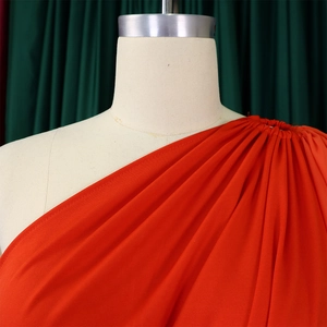 Detail of orange one-shoulder jumpsuit featuring pleated fabric and elegant texture