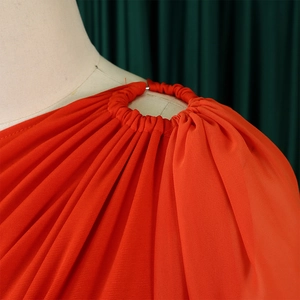 Detail view of the metal ring connector and elegant pleated design on the orange jumpsuit