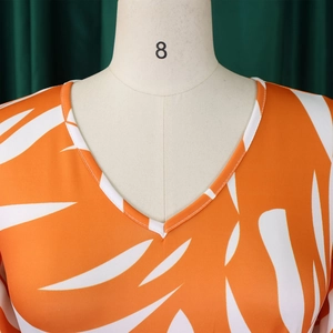 Détail du col en V sur robe orange à imprimé de feuilles tropicales blanches