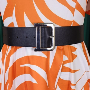 Détail d'une large ceinture en cuir noir avec boucle métallique en D sur une robe fleurie
