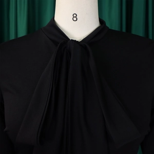 Detail of elegant black blouse featuring tie-neck bow and smooth puff sleeve fabric