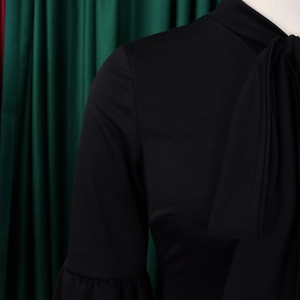 Detail showing the elegant tie-up bow neckline and ruffled sleeves on a black dress