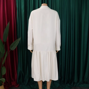 Detail view of the drop shoulder design and ruffled hem on an off-white maxi dress