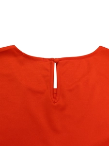 Detailed view of the round neckline and fabric button on a bright orange-red summer top
