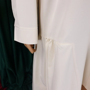 Close-up of cream white long sleeve dress showing woven fabric texture and pleated detail