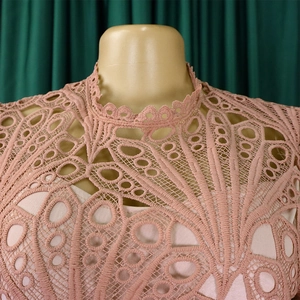 Close-up of pink hollow lace fabric with intricate floral patterns and wavy neckline