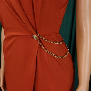 Detail der Taille mit goldfarbenem Knopf und doppelter Metallkettendekoration am Jumpsuit
