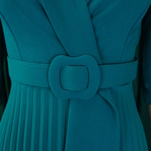 Détail d'une robe bleu canard avec jupe plissée et ceinture à boucle carrée de la même couleur