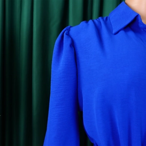Detail of royal blue long sleeve jumpsuit featuring pleated puff shoulders and classic collar