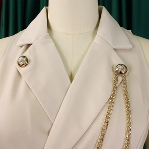 Detail of lapel collar with golden embossed buttons and hanging chain on beige jumpsuit