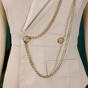 Detailed view of beige jumpsuit featuring gold chain accents and embossed portrait buttons