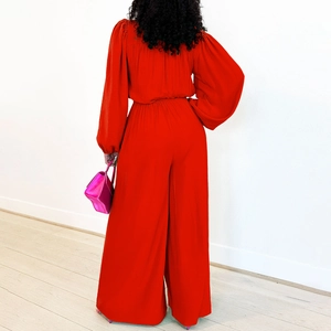 Back view of a red long sleeve high waist jumpsuit with wide leg pants and a pink handbag