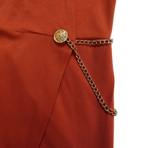 Detail des rostroten Jumpsuits mit goldenen Reliefknöpfen und dekorativen Metallketten