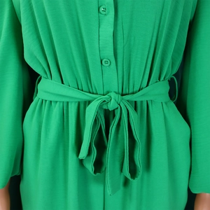 Detail view of the green jumpsuit showing the button closure and waist tie with bow
