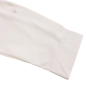Detail of the cuff featuring a round button on a cream-colored long sleeve dress