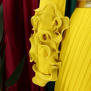 Détail des manches plissées à volants sur une combinaison jaune avec ceinture dorée