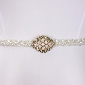 Detail view of a white double-row pearl belt with a gold rhinestone buckle on white fabric