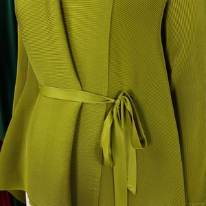 Dettaglio della trama in tessuto plissettato verde e cintura annodata su un top da donna
