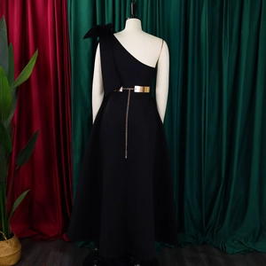 Detail of black one-shoulder evening gown with large bow and gold mirror belt tassels