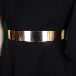 Close-up of a wide polished gold metal belt showing mirror finish on black dress