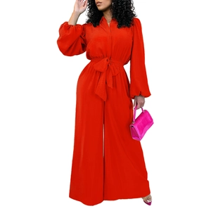 Detail of orange wide-leg jumpsuit featuring waist bow tie and long lantern sleeves