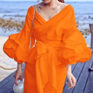 Detail of bright orange off-shoulder wrap top with puff sleeves and waist tie bow