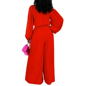 Detail view of the vibrant red wide-leg jumpsuit showing gathered waist and lantern sleeves