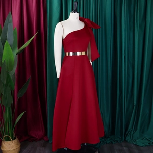 Detail of burgundy one-shoulder gown with large bow and gold belt on mannequin