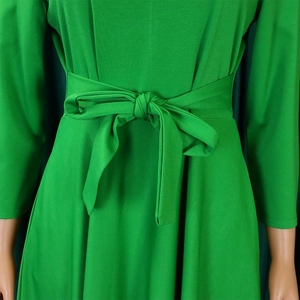 Detail of a grass green dress featuring a matching waist tie bow and knitted fabric texture