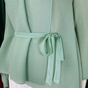 Dettaglio del cardigan a pieghe verde chiaro con sottili pieghe a fisarmonica e cintura