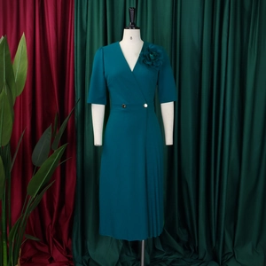Detailed view of the dark green V-neck dress featuring golden buttons and pleated accents