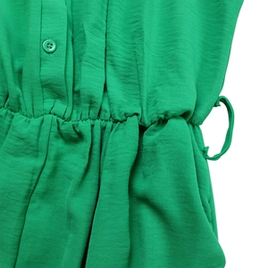 Detail of green long sleeve jumpsuit featuring elastic waist, buttons and textured fabric