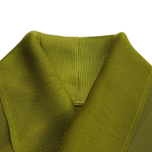 Dettaglio del tessuto plissettato verde oliva con pieghe verticali e scollo incrociato