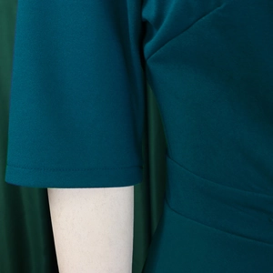 Detailed view of the short sleeve cuff and side stitching on dark green pleated dress