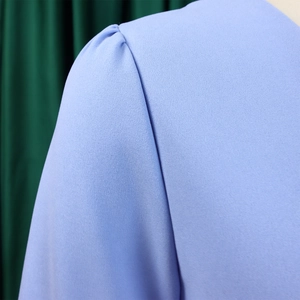 Close-up of pleated shoulder detail and fabric texture on light blue V-neck dress
