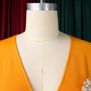 Detail eines gelben V-Ausschnitt-Kleides mit eleganter silberner Perlen-Strass-Brosche