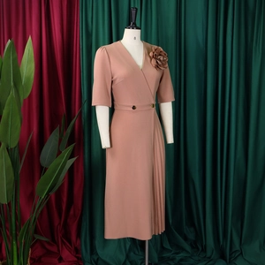 Detail view of pink V-neck dress with side pleats and a floral brooch on a mannequin
