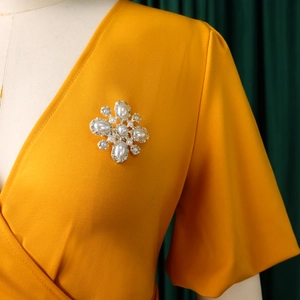 Detailansicht einer Vintage-Perlenbrosche mit Kristallen auf einem gelben V-Ausschnitt Kleid