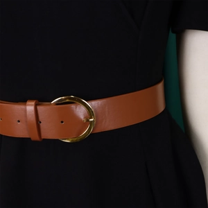 Close-up of brown leather waist belt with round gold metal buckle on black fabric