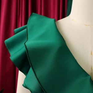 Macro shot of dark green ruffled hem with fine stitching on smooth satin evening dress