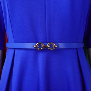 Dettaglio di un abito in maglia blu reale con cintura sottile in pelle e fibbia a catena oro