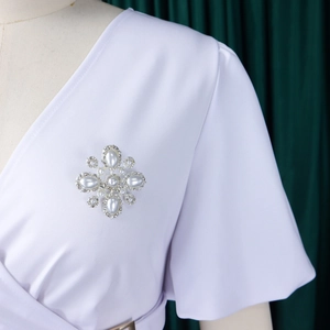 Nahaufnahme einer silbernen Kreuzbrosche mit Perlen und Kristallen auf weißem Kleid