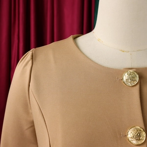 Detail of the khaki round neck blazer featuring elegant gold crest buttons and ruffle trim