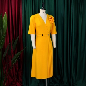 Detail of V-neck yellow dress featuring a large 3D floral brooch and side pleats